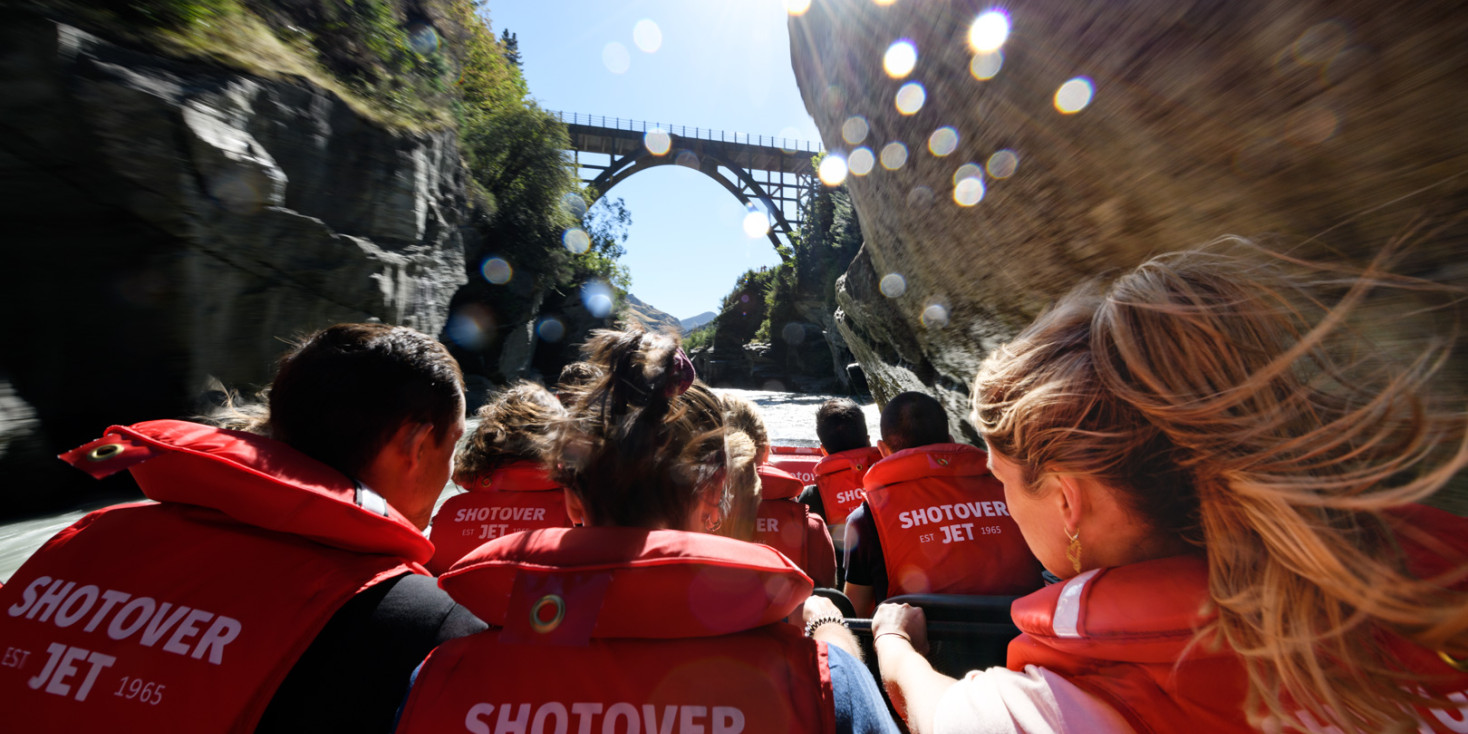 Shot of passengers from behind on shotover jet travelling toward bridge